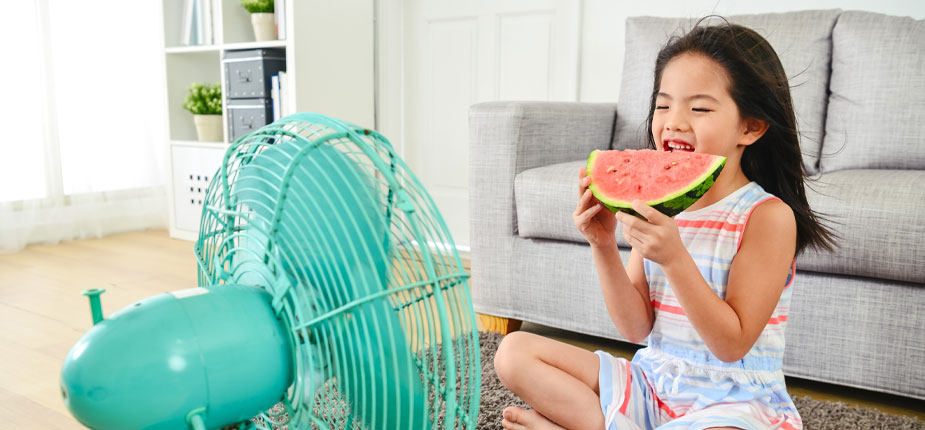 Little girl eating a watermelon in front of a fan